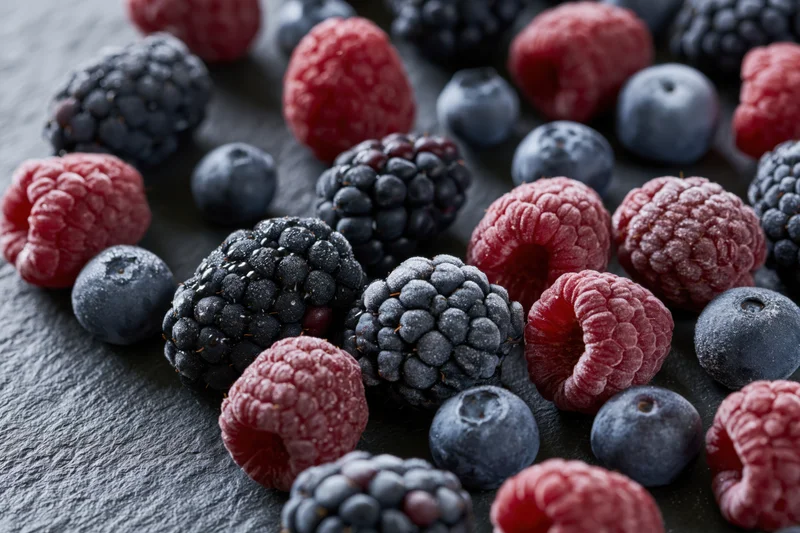 Frozen mixed berries arranged in close-up flat lay on dark slate surface
