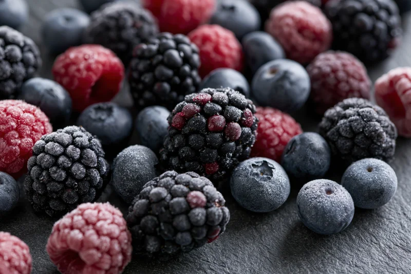 Frozen mixed berries arranged in a closeup flat lay on a dark stone surface