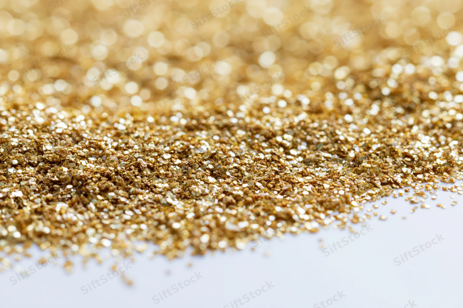 Gold glitter scattered densely on a white surface with bokeh effect and copyspace