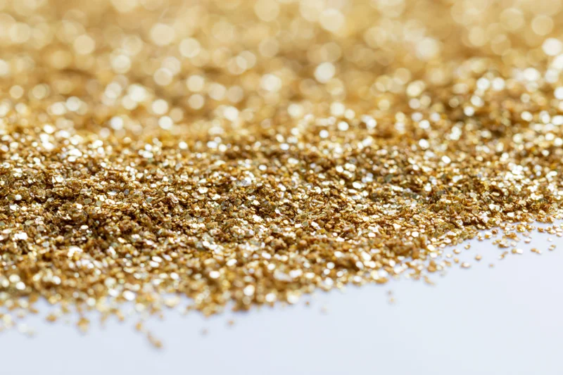Gold glitter scattered densely on a white surface with bokeh effect and copyspace