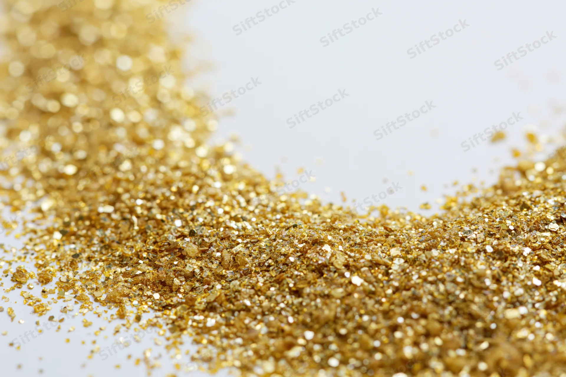Gold glitter scattered densely on a white surface in a flat lay composition