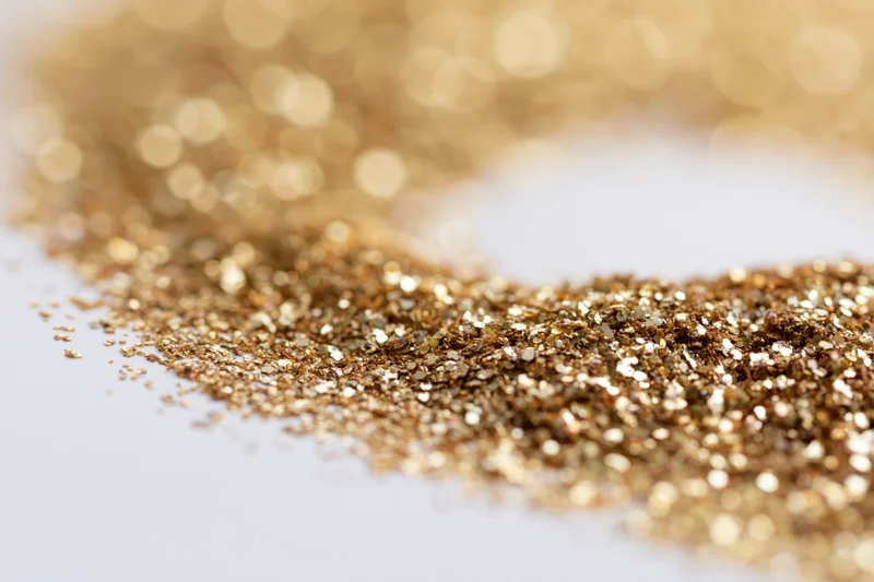 Gold glitter scattered densely on white surface with bokeh background