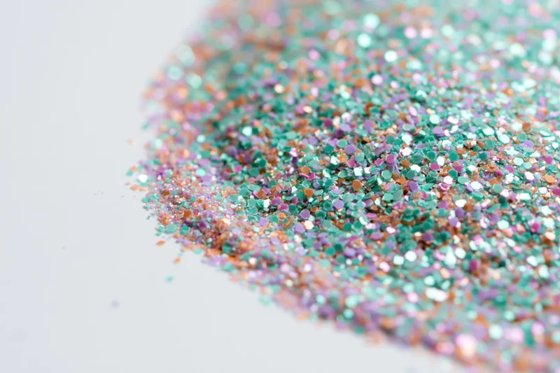 Iridescent glitter scattered densely on white surface in flat lay view