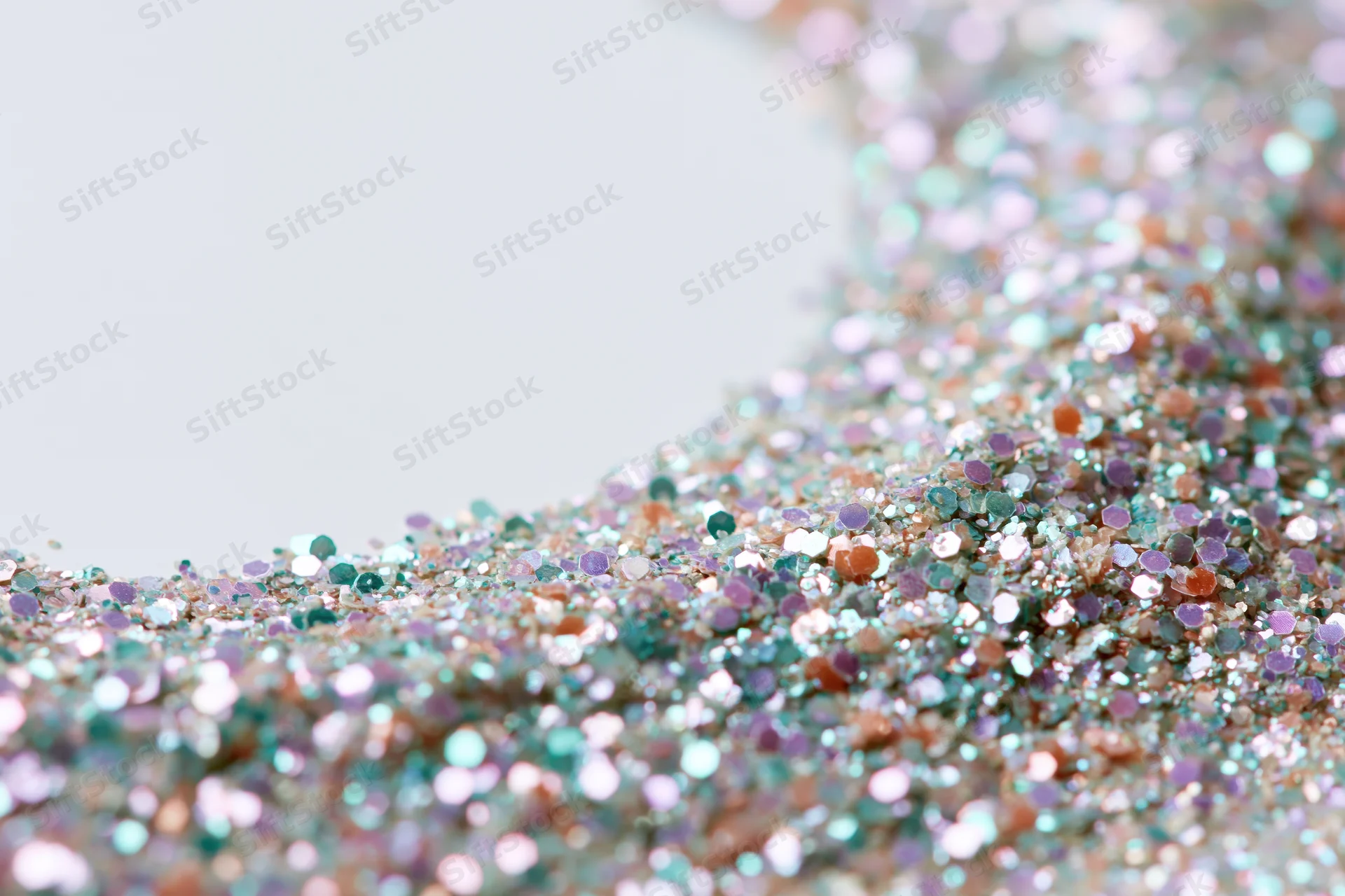 Iridescent glitter scattered densely on a white surface with shallow depth of field and copyspace on the left
