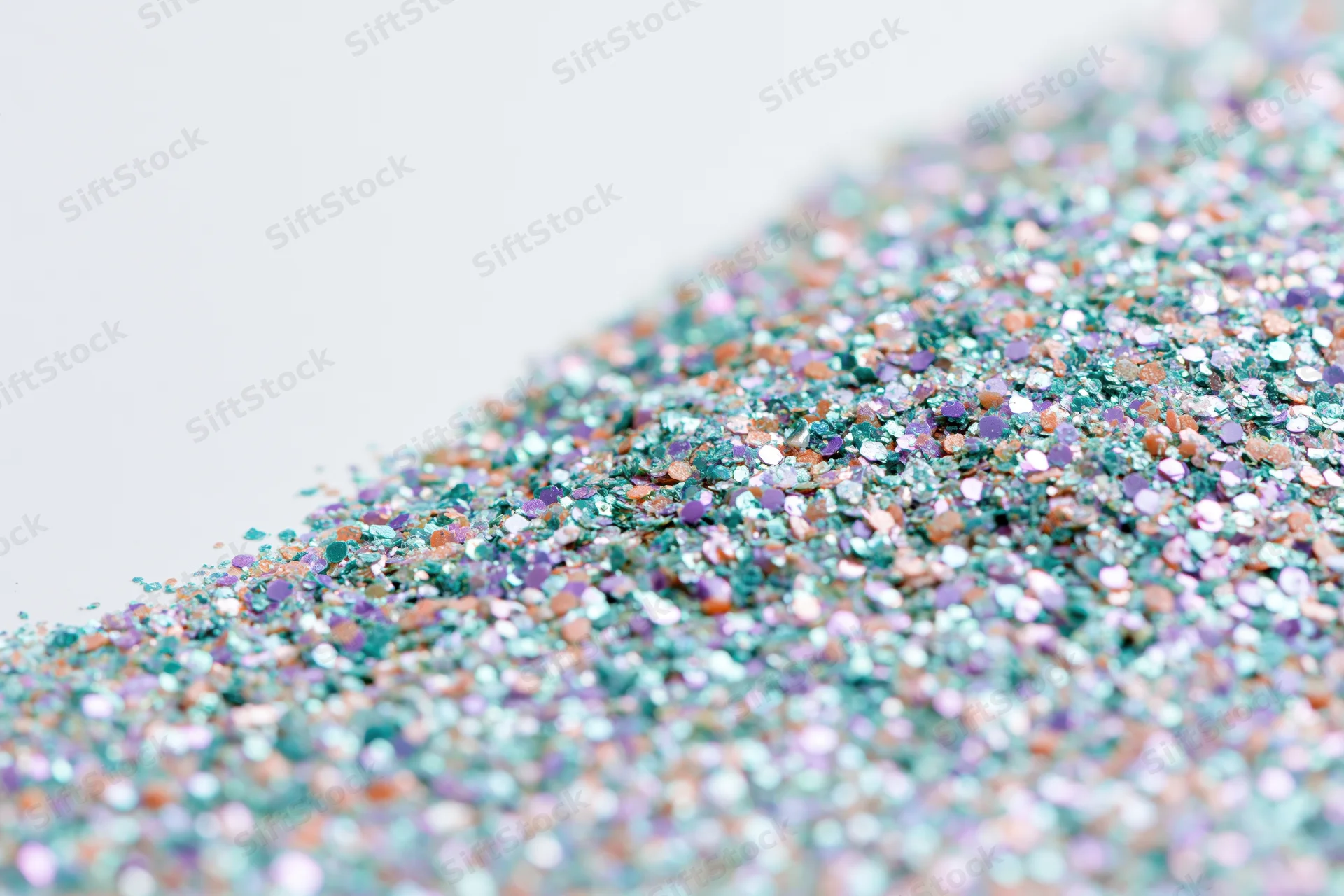 Iridescent glitter scattered densely on a white surface in a close-up flat lay