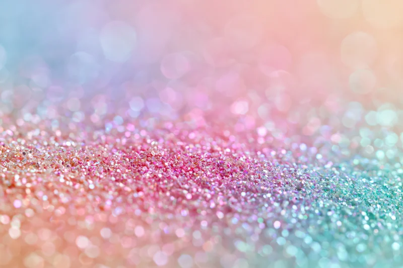 Close-up of iridescent glitter surface with pastel pink and blue hues and bokeh effect