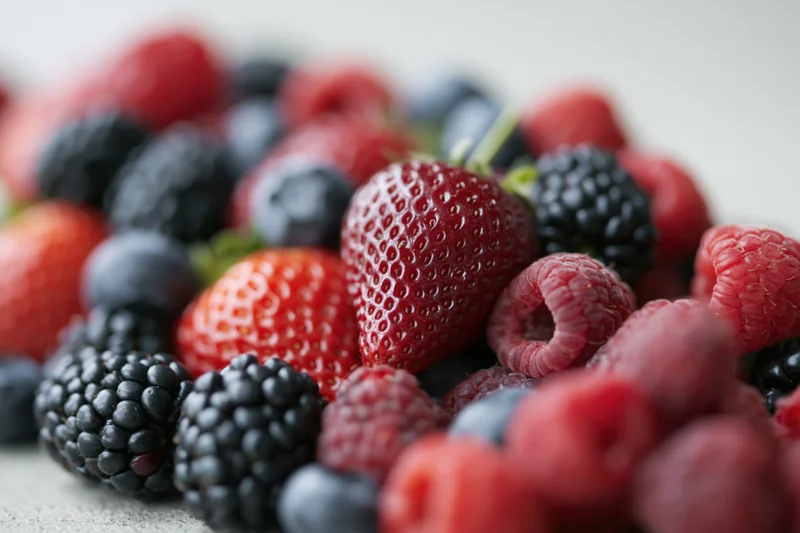 Close-up of mixed fresh berries including strawberries raspberries blackberries and blueberries on a light surface