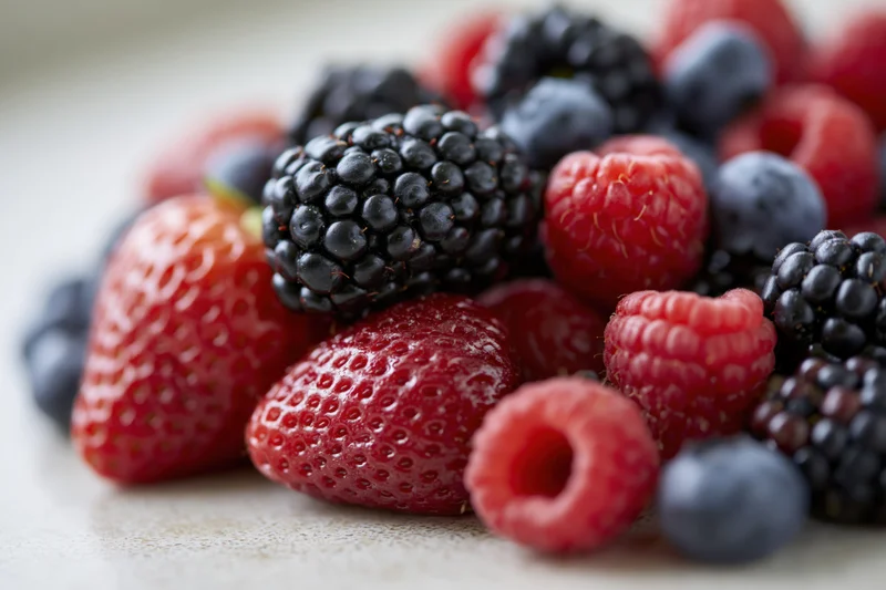 Close-up of mixed fresh berries including strawberries raspberries blackberries and blueberries piled together on a light surface