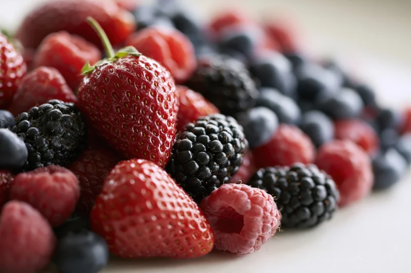 Close-up of mixed fresh berries including strawberries raspberries blackberries and blueberries on a white surface