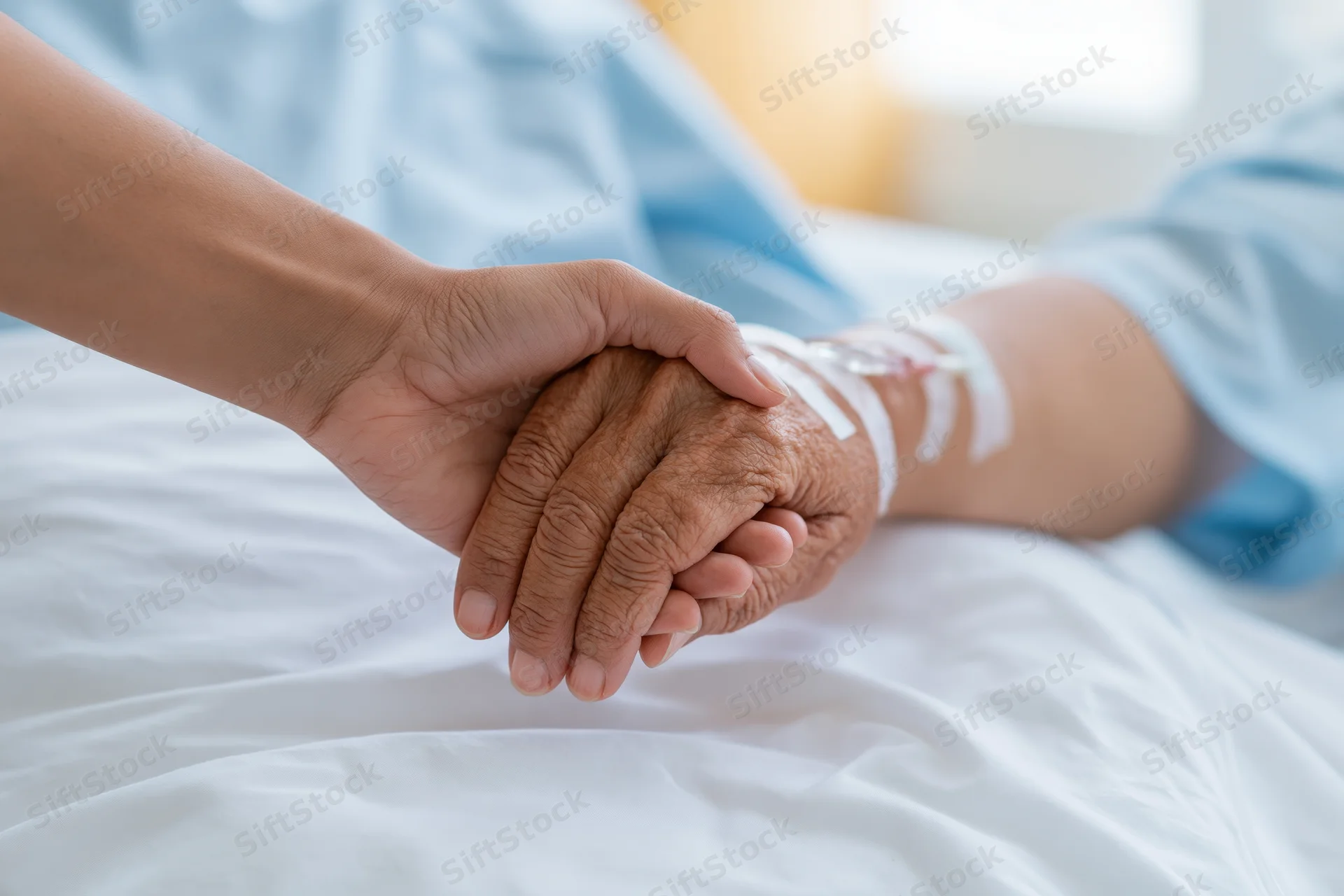 Younger person holding elderly patient's hand in hospital bed
