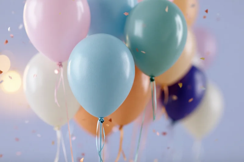Cluster of colorful latex balloons floating with confetti against a soft glowing background