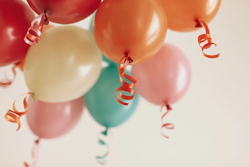 Cluster of colorful party balloons with curling ribbon streamers floating against a light background