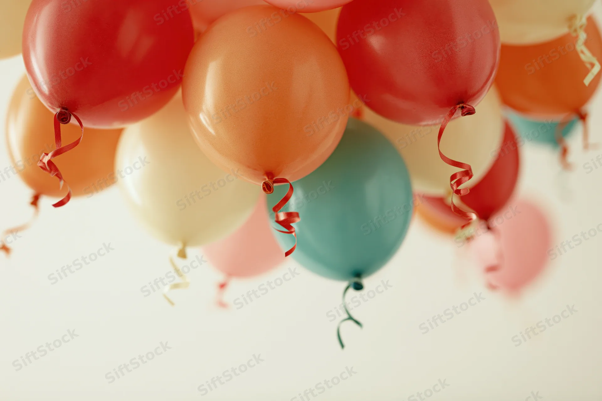 Cluster of colorful party balloons with curling ribbon streamers floating against a soft light background