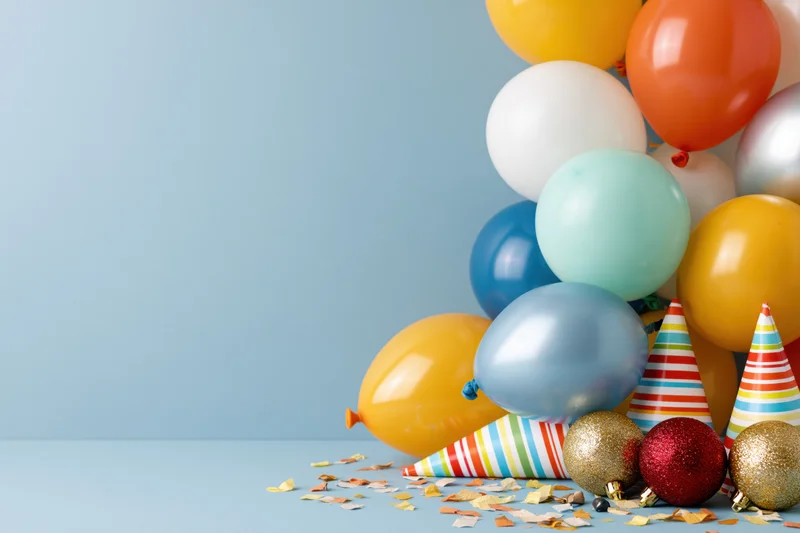 Colorful party balloons and hats with confetti on a blue surface