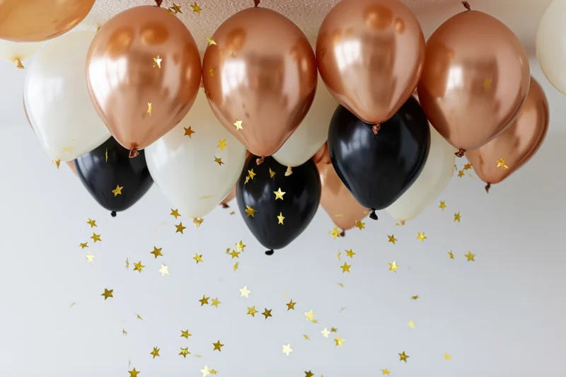 Cluster of copper, black and white latex balloons floating near ceiling with gold star confetti falling below