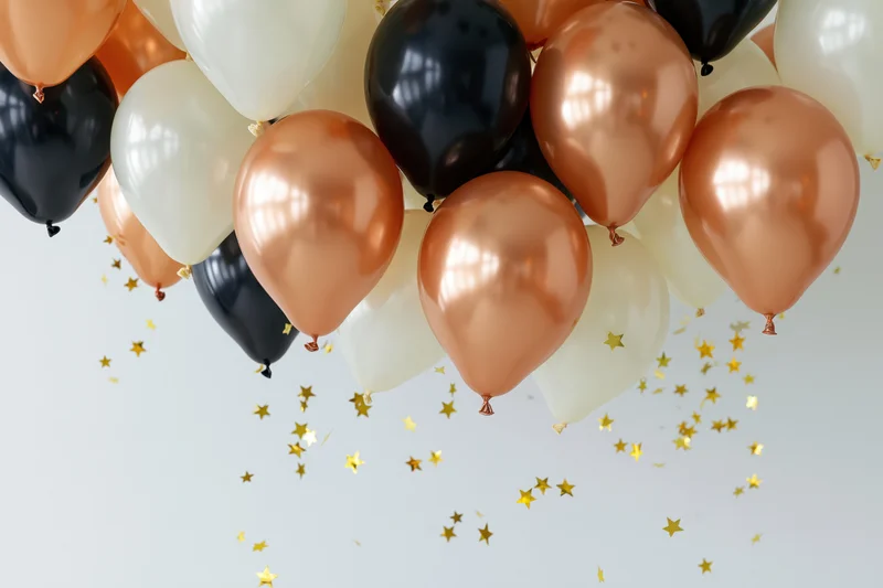 Cluster of copper black and white latex balloons floating with gold star confetti against light background