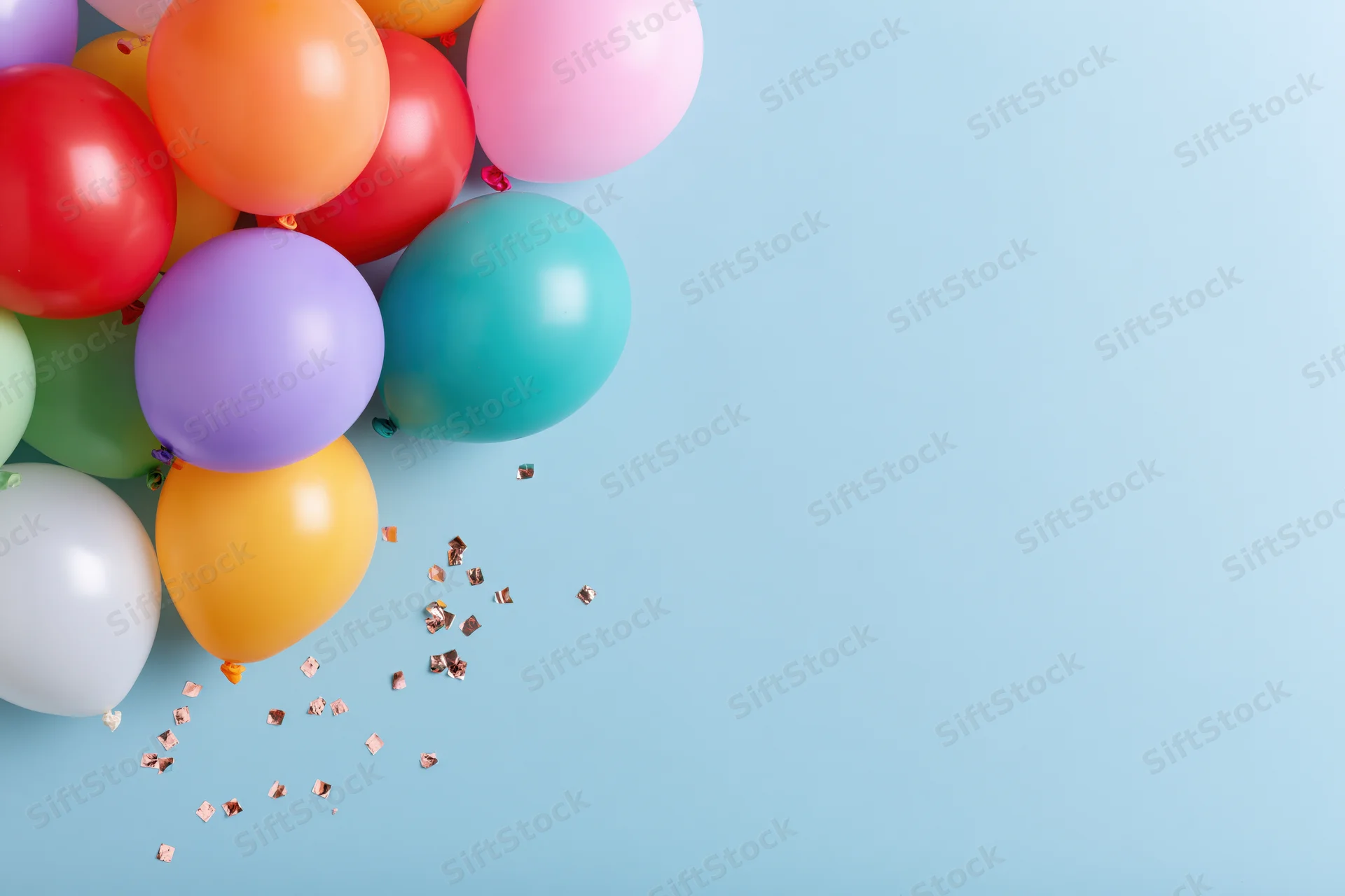 Multicolored latex balloons and confetti arranged in cluster on light blue surface with copyspace