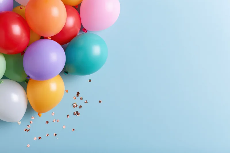 Multicolored latex balloons and confetti arranged in cluster on light blue surface with copyspace
