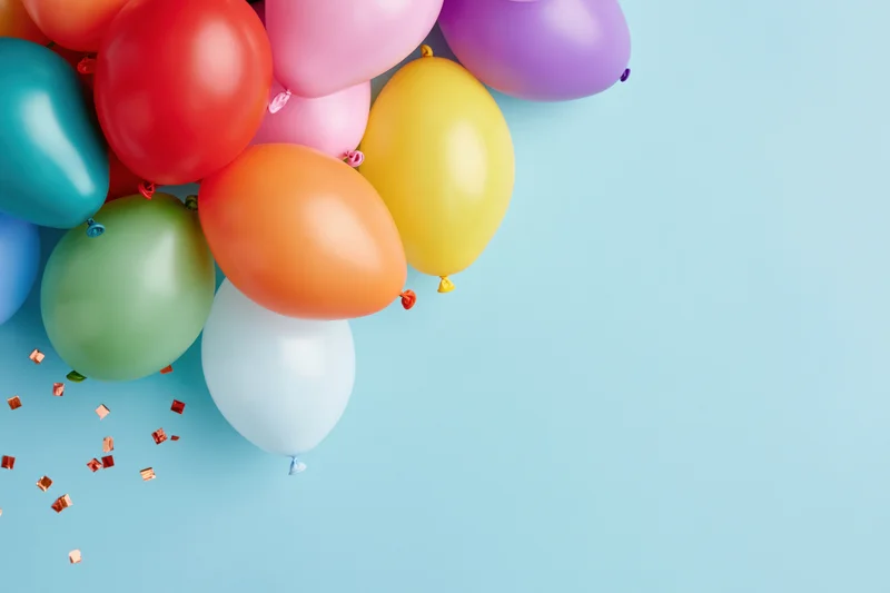 Cluster of multicolored latex balloons with confetti on light blue background