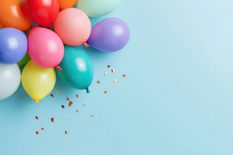 Cluster of multicolored latex balloons with scattered confetti on light blue surface