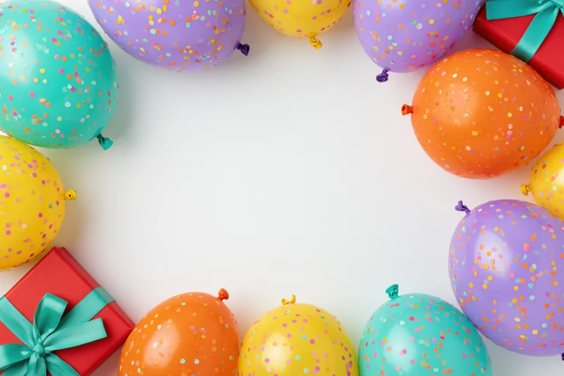 Colorful confetti balloons and wrapped gift boxes arranged in a border around white copyspace