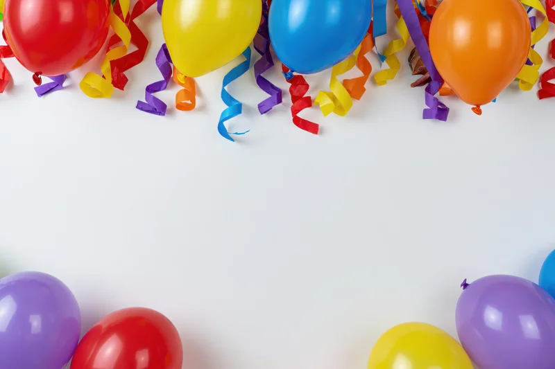 Colorful latex balloons and curled paper streamers arranged along the top and bottom edges of a white surface, leaving central copyspace