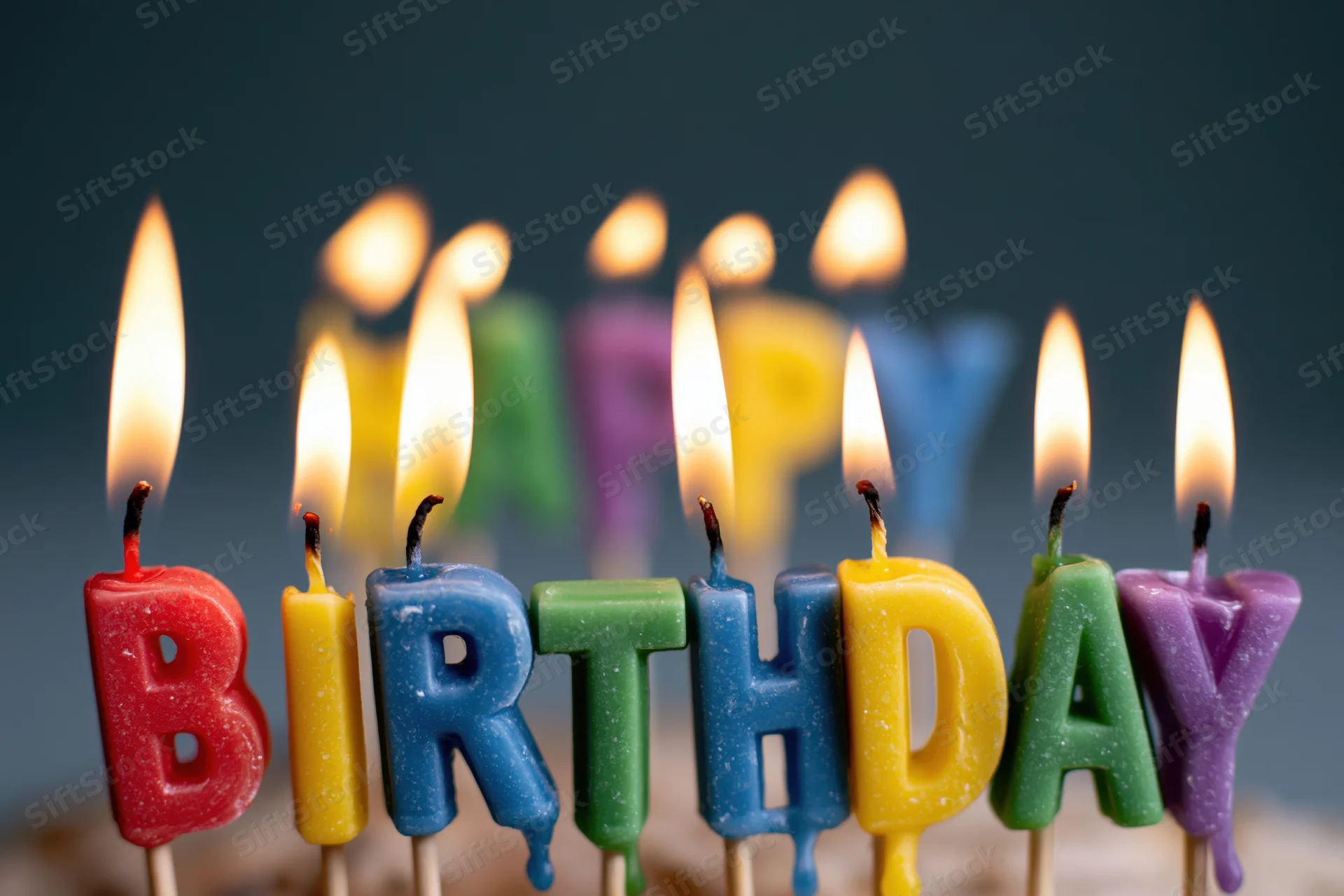 Colorful letter-shaped birthday candles spelling birthday on a cake, lit with flames, close-up view against a dark background with shallow depth of field and copyspace on the sides