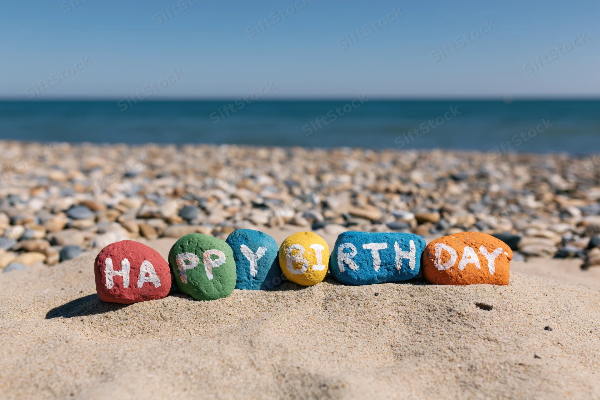 Colorful painted stones spelling happy birthday on sandy beach by ocean