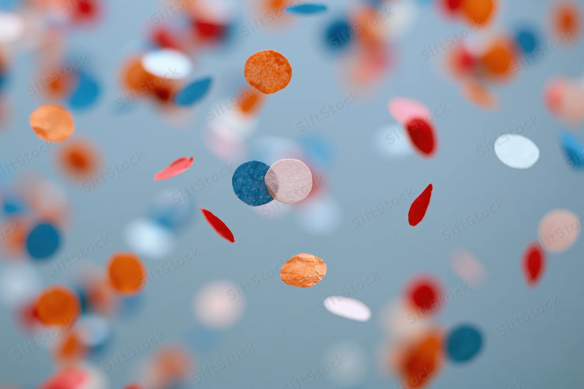 Colorful paper confetti pieces floating midair against a soft blue background