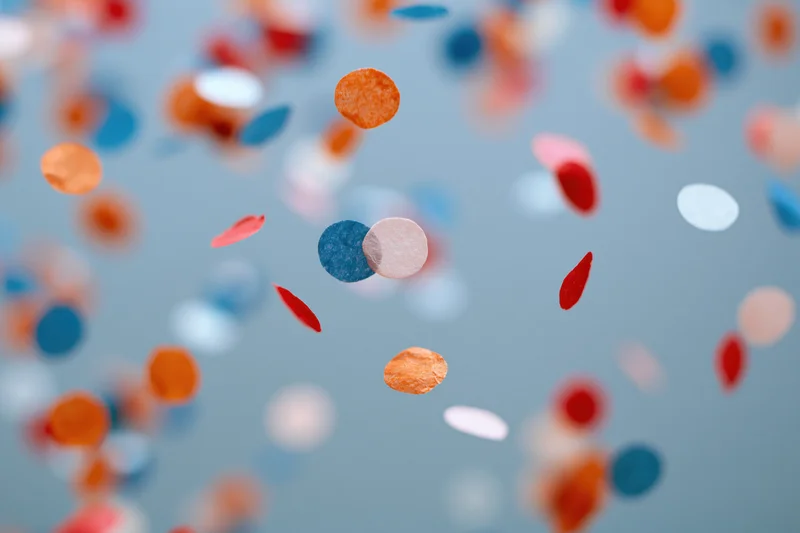 Colorful paper confetti pieces floating midair against a soft blue background