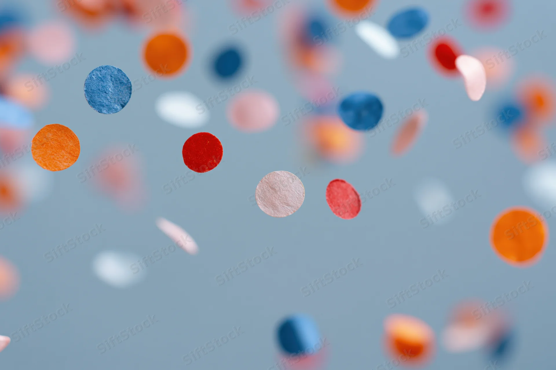 Colorful paper confetti pieces floating midair against a soft blue background