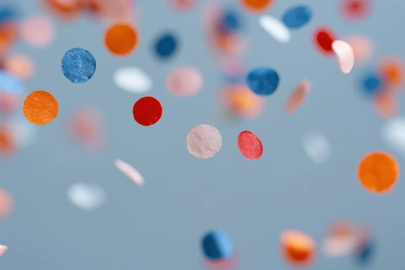 Colorful paper confetti pieces floating midair against a soft blue background