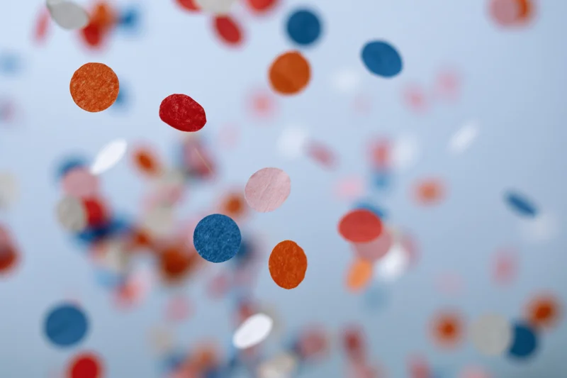 Colorful paper confetti pieces suspended midair against a light blue background