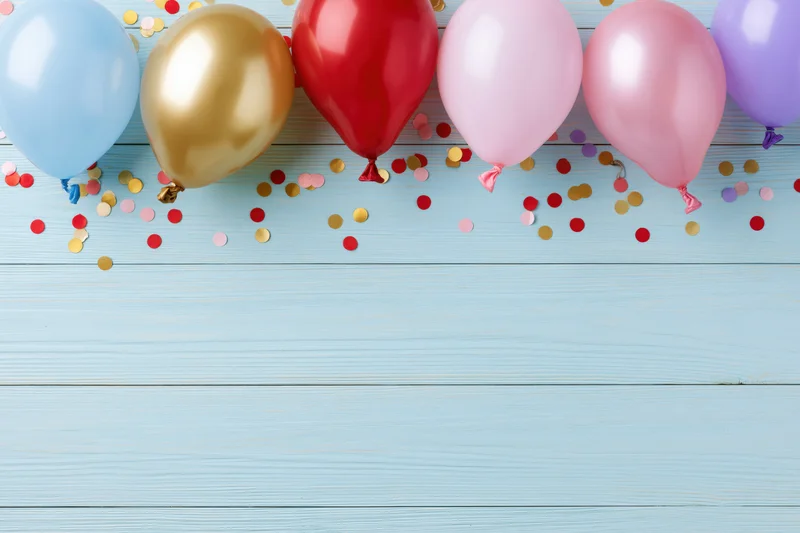 Colorful party balloons and scattered confetti on a light blue wooden surface
