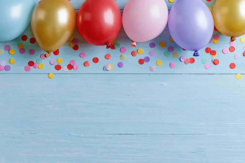 Colorful party balloons and scattered confetti on a blue wooden surface