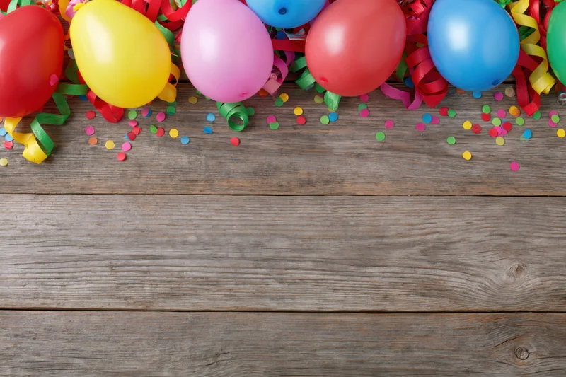 Colorful party balloons and streamers with confetti on a rustic wooden tabletop, leaving copyspace below