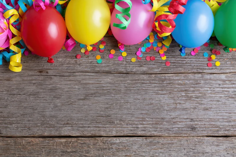 Colorful party balloons and streamers with confetti on wooden surface, top view with copyspace