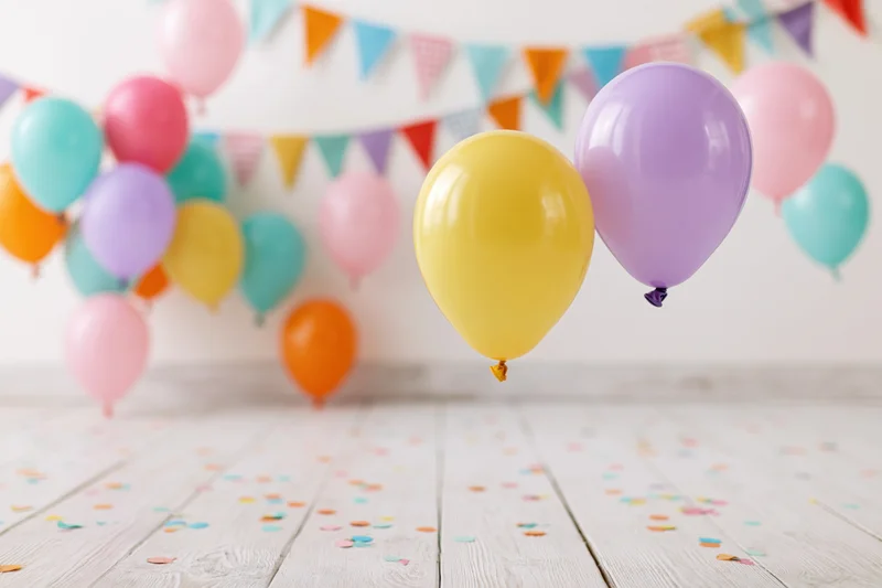 Colorful balloons floating above a wooden floor scattered with confetti and a banner in the background