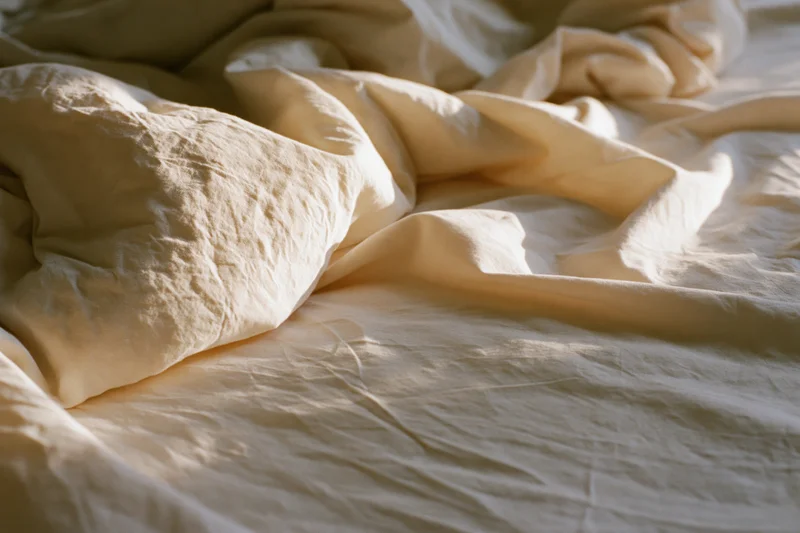 Crumpled white linen sheets draped over unmade bed in soft morning light