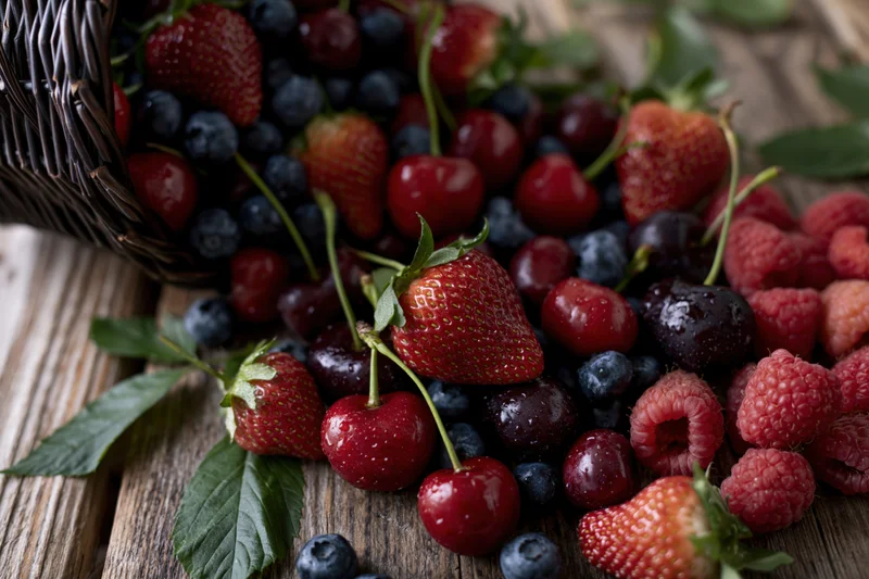 Dark wicker basket tipped over spilling fresh berries onto wooden surface