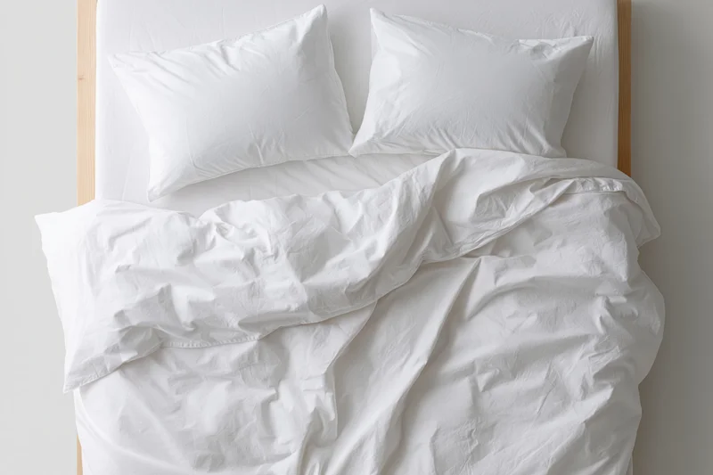 Unmade double bed with white cotton duvet and two pillows, headboard visible, bedroom setting