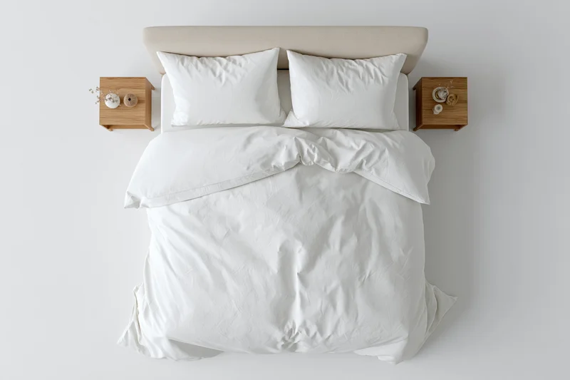 Overhead view of a double bed with white linen and four pillows flanked by wooden nightstands in a minimalist bedroom