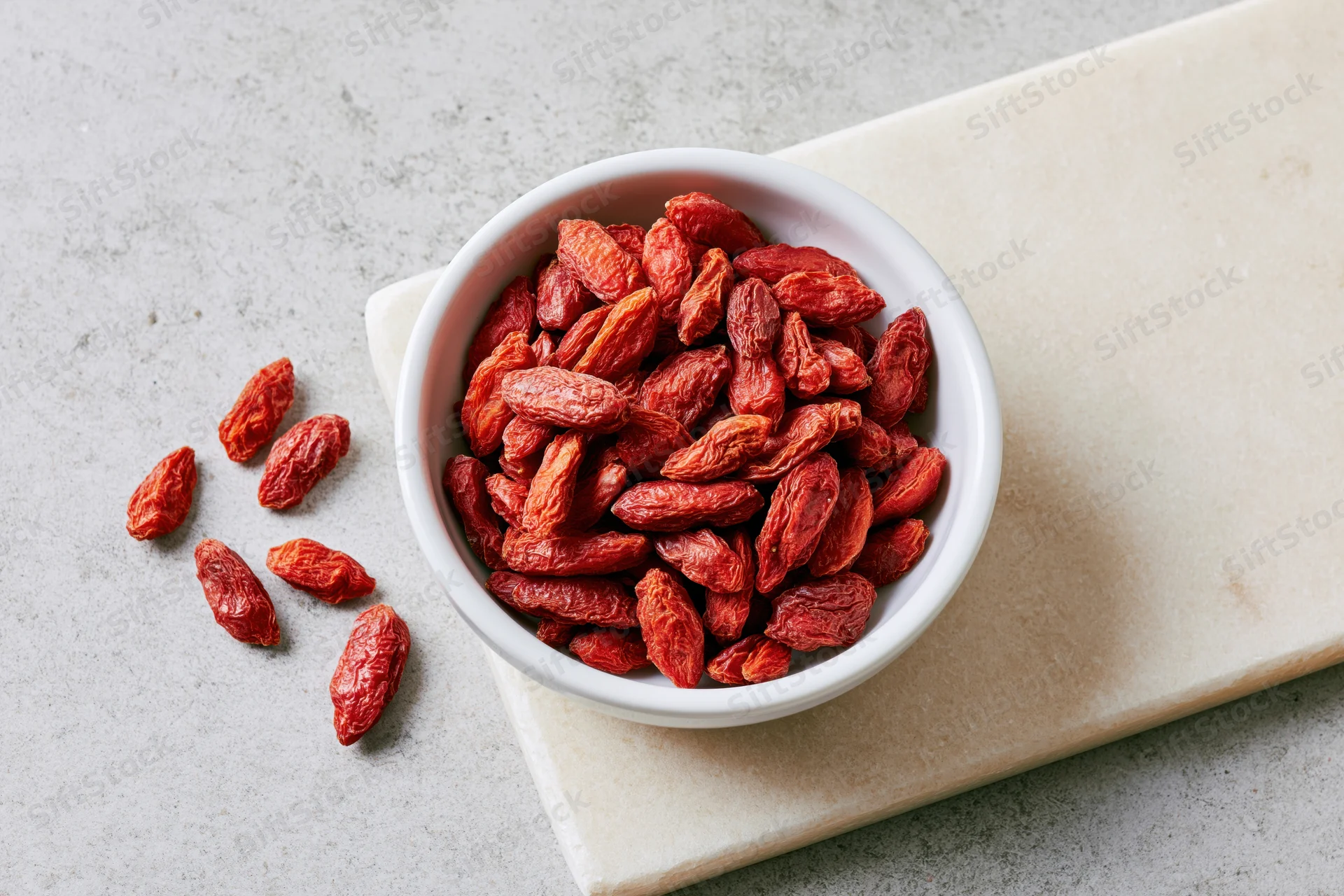 Dried goji berries in a white ceramic bowl on a marble cutting board