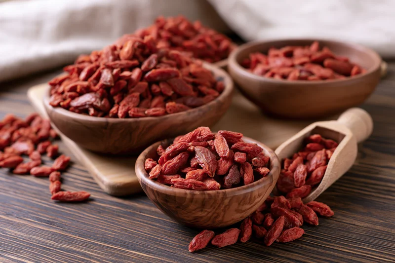 Dried goji berries in rustic wooden bowls and a scoop on a dark wooden table