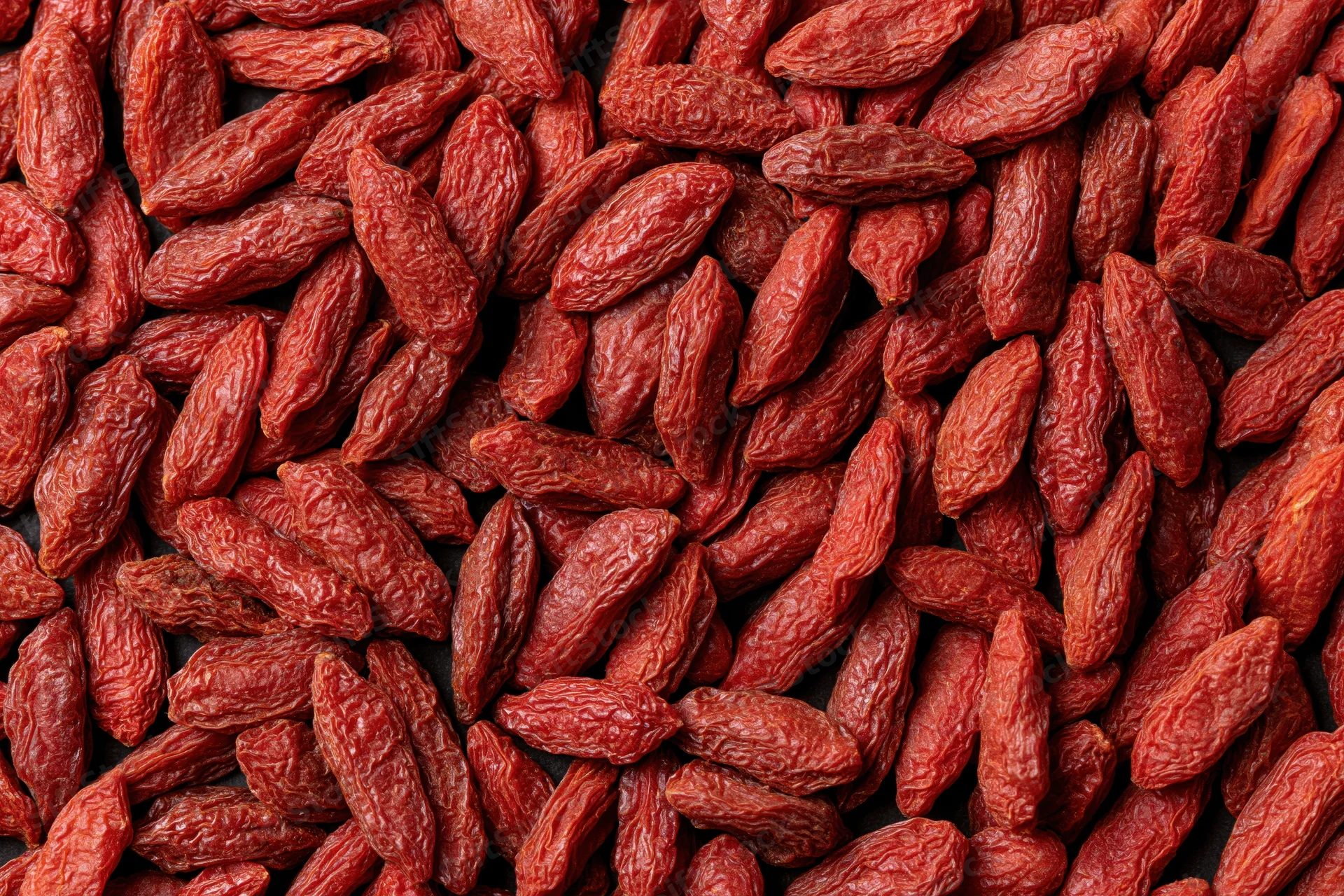 Dried goji berries scattered across a dark flat surface