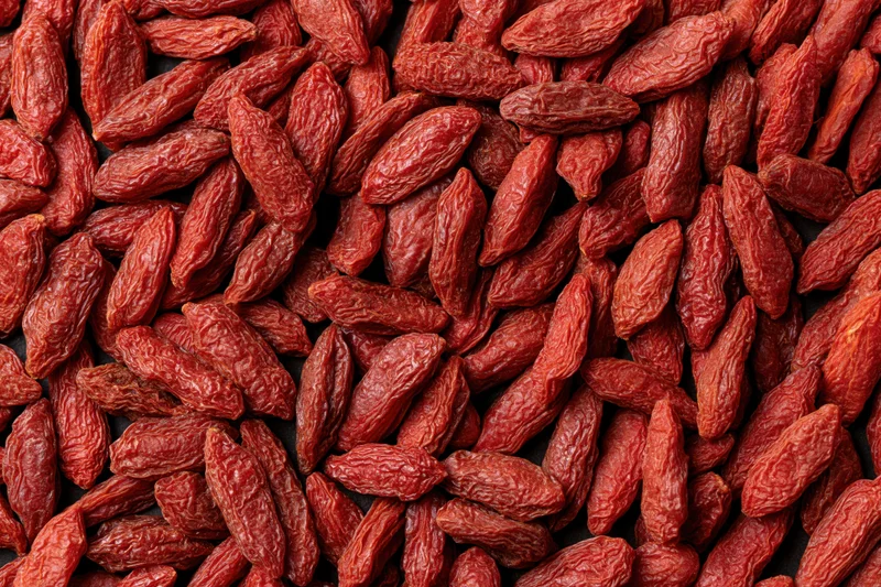 Dried goji berries scattered across a dark flat surface