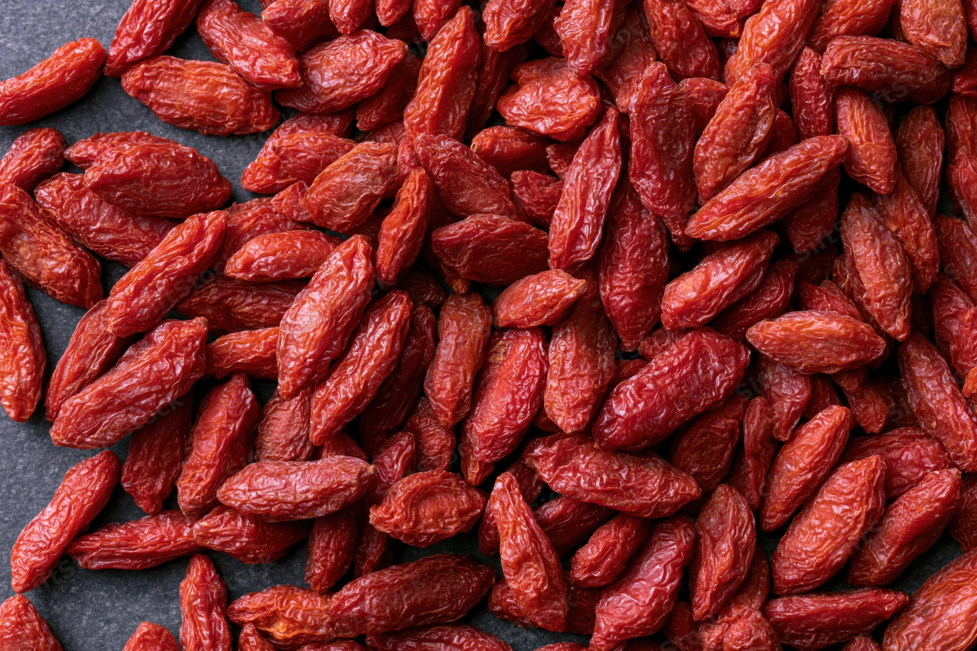 Dried goji berries scattered across a dark surface
