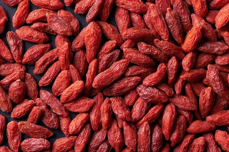 Dried goji berries scattered across a dark surface in a close-up still life