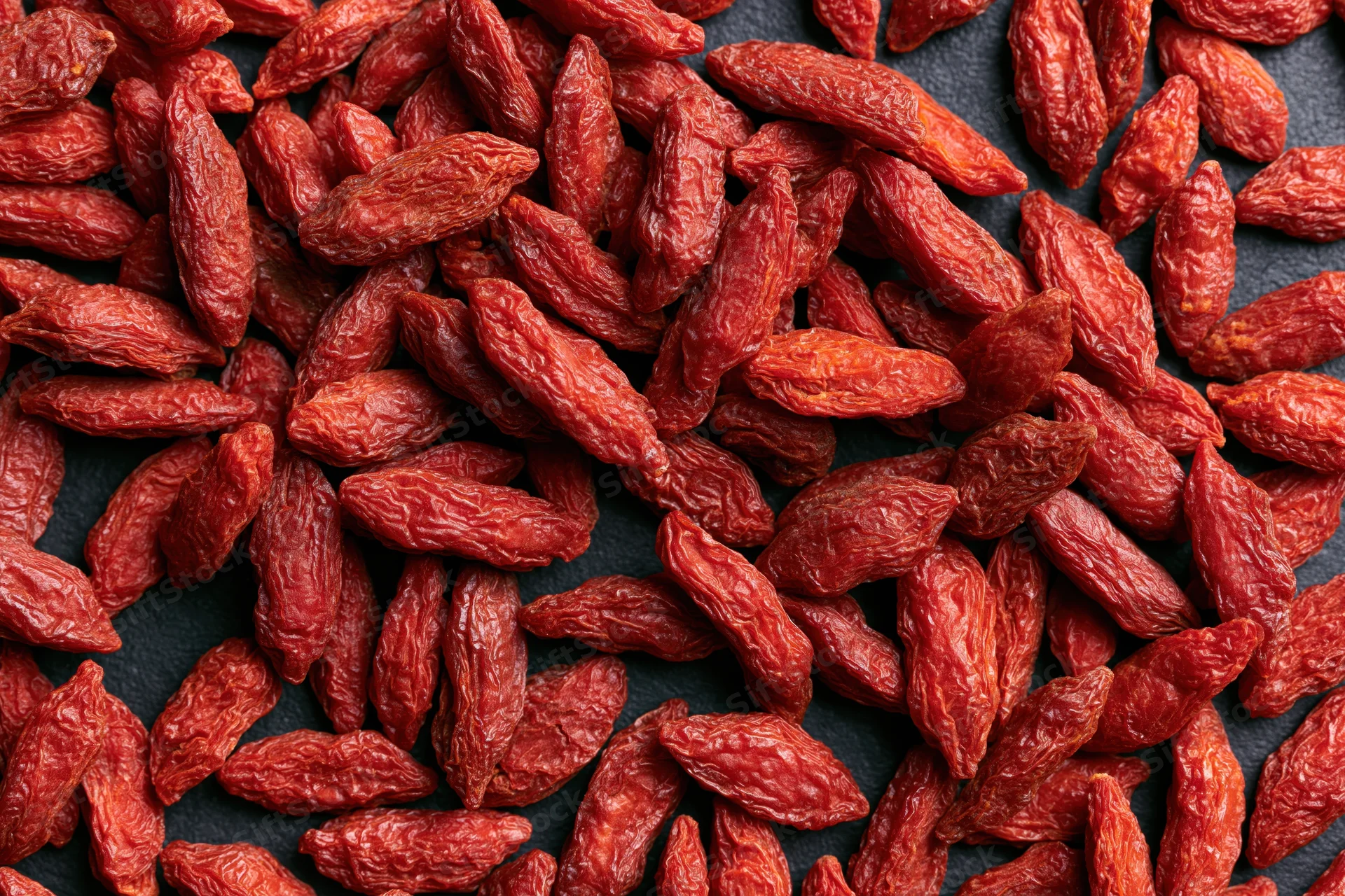 Dried goji berries scattered across a dark surface in closeup view