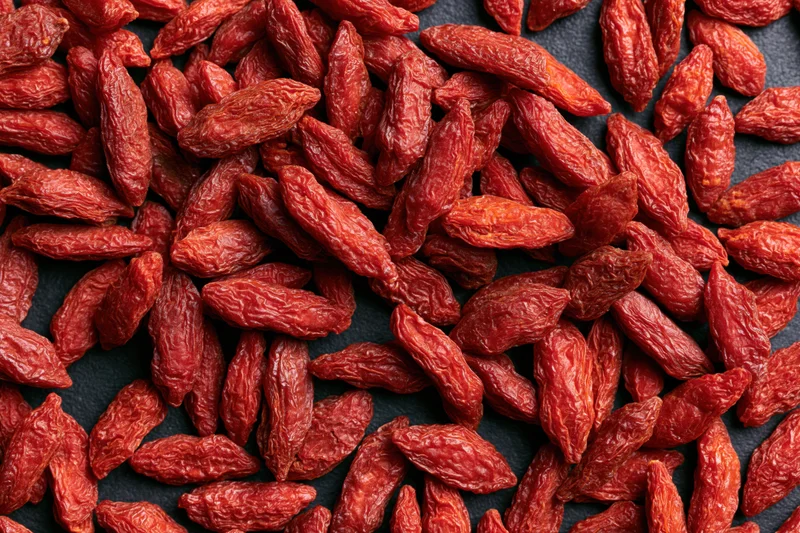 Dried goji berries scattered across a dark surface in closeup view